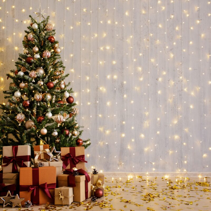 Árbol de Navidad decorado con bolas, luces y regalos. Foto: Adobe Stock.